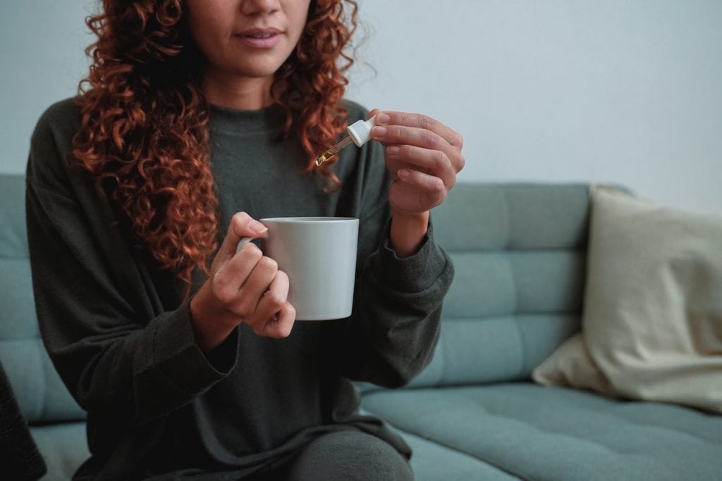 Woman adding CBD drops to tea cup