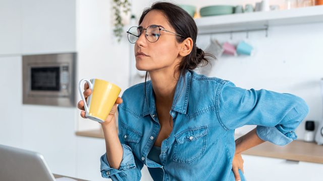 A tired woman with back pain looking uncomfortable as she sits in front of a computer