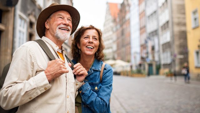 A man and woman smile as they look down the road at their vacation destination.