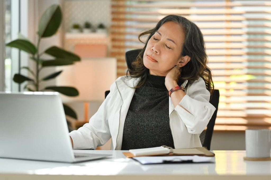 A woman sitting at her desk rubbing her sore neck