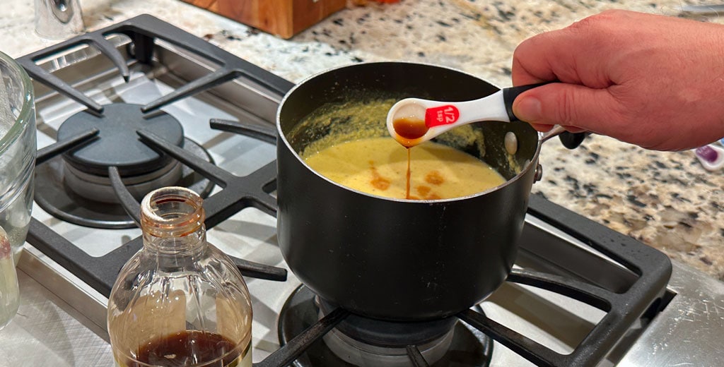 Adding vanilla extract to warm eggnog custard off the heat to finish flavor and aroma.