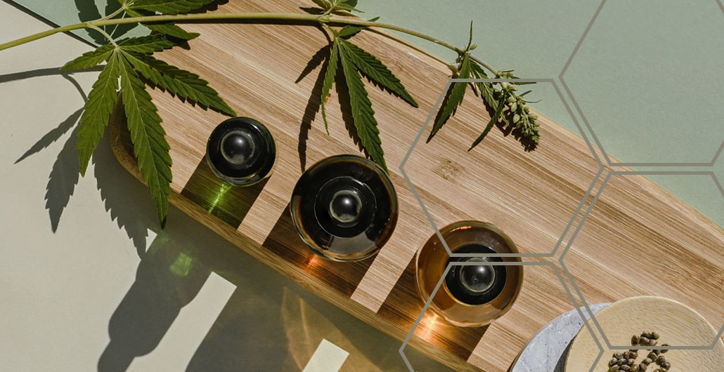 Hemp Oil glass bottles on a bamboo board with a hemp leaf hanging above them.