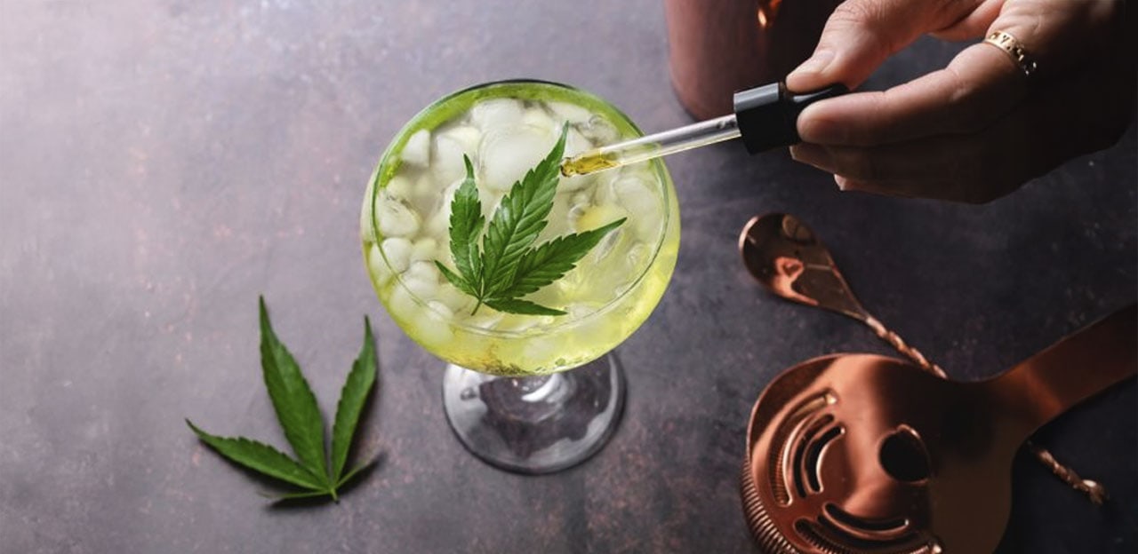 Eyedropper pouring CBD Oil on a glass with hemp leaf