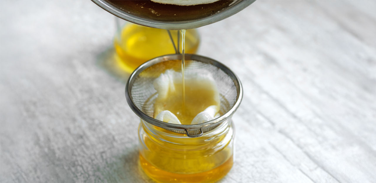 CBD Oil being pour to glass with a strainer on a white wooden table top