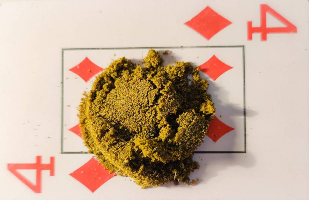Close-up of amber-brown decarboxylated kief mounted on a 4 of hearts playing card, illustrating its dry, powdery texture and golden brown color change after heat activation.