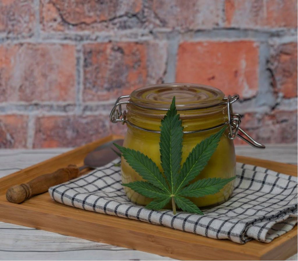 Cannabis-infused mixture stored in an airtight glass jar on a kitchen tray with a cannabis fan leaf in the foreground.