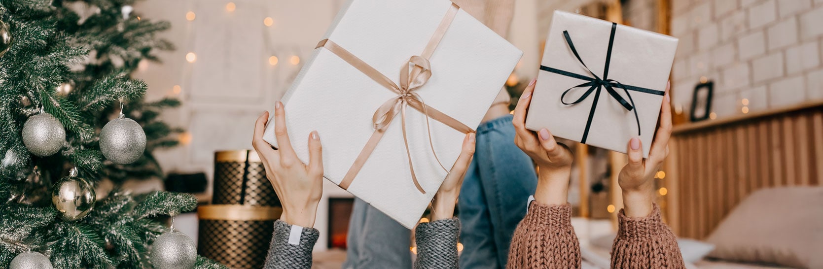 Hands holding wrapped holiday gifts near a decorated Christmas tree, symbolizing thoughtful gift selection based on personal experience.
