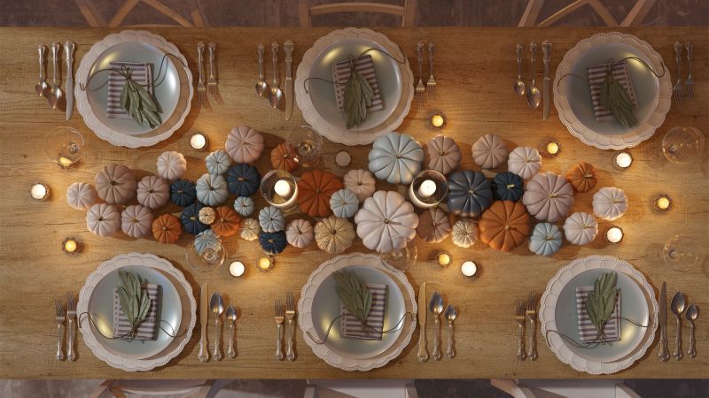 Top-down view of an elegant Thanksgiving table setting decorated with neutral and colorful mini pumpkins, candles, and neatly arranged dinner plates for a festive holiday meal.
