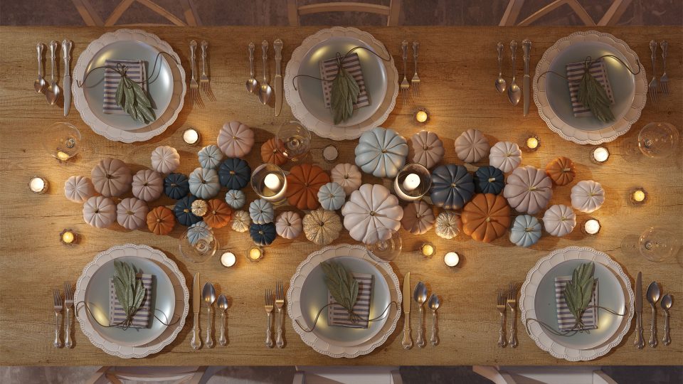 Top-down view of an elegant Thanksgiving table setting decorated with neutral and colorful mini pumpkins, candles, and neatly arranged dinner plates for a festive holiday meal.