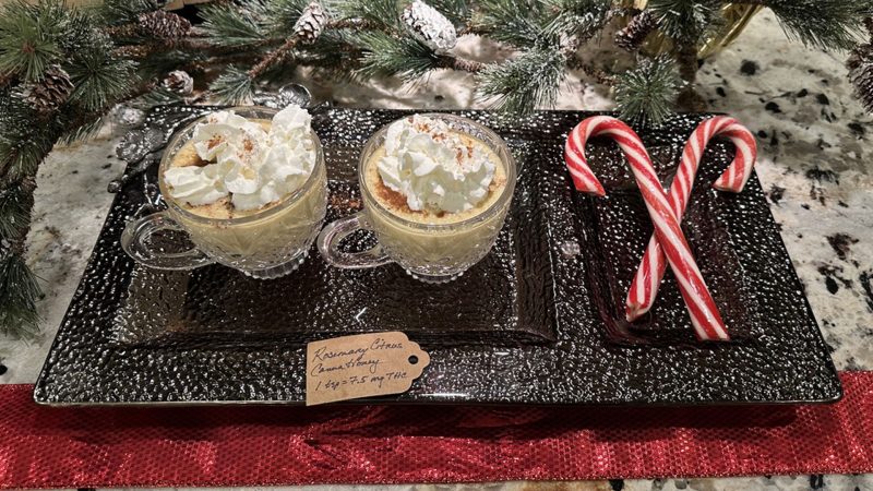Cannabis-infused eggnog served in glass mugs topped with whipped cream and nutmeg, styled on a festive holiday tray with candy canes.