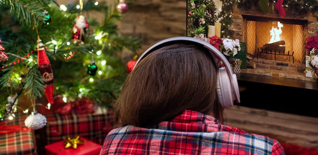 Person wearing headphones relaxing near a television streaming the CannaYule Log with holiday lights in the background